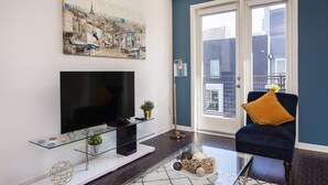 A living room with a flat-screen TV, glass coffee table, and a blue armchair with a mustard-colored pillow. - New Downtown LA Luxury Jr. Penthouse (Los Angeles)