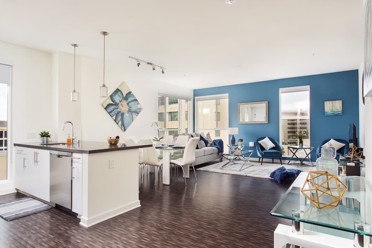 Eine moderne Küche mit Kochinsel, Essbereich mit weißer Möbel und ein Wohnzimmer mit blauen Wänden und dunklem Holzboden.