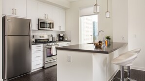 A modern kitchen with white cabinets, stainless steel appliances, and a central island with bar stools. - New Downtown LA Luxury Jr. Penthouse (Los Angeles)
