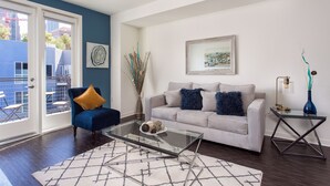 A living room with a glass coffee table, a sofa with decorative pillows, a vase with branches, and a framed picture on the wall. - New Downtown LA Luxury Jr. Penthouse (Los Angeles)