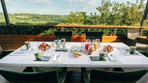 Een ontbijttafel met een prachtig uitzicht, inclusief een fruitschaal, croissants en diverse drankjes.
