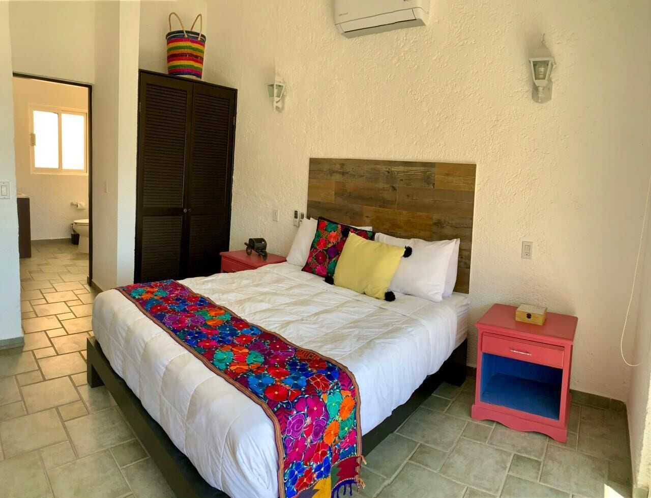 Quarto com cama, mesa de cabeceira, guarda-roupa e ar condicionado fixado na parede.