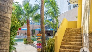 A pathway leading to a pool area with palm trees, a signpost with amenities, and a staircase. - Antigua de Cabo (Cabo San Lucas)