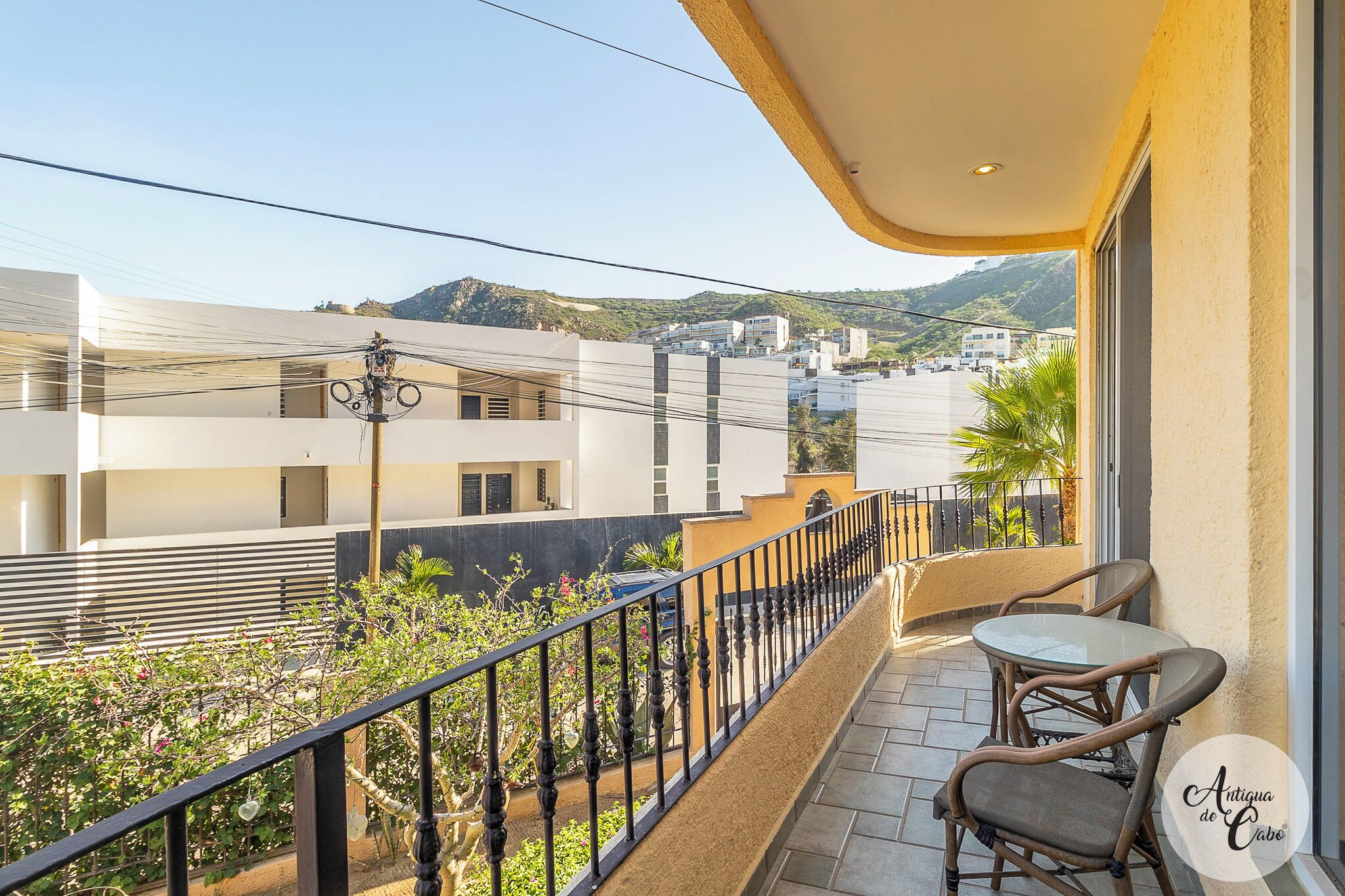 A balcony with a view of a residential area, a table and chairs, and a railing.