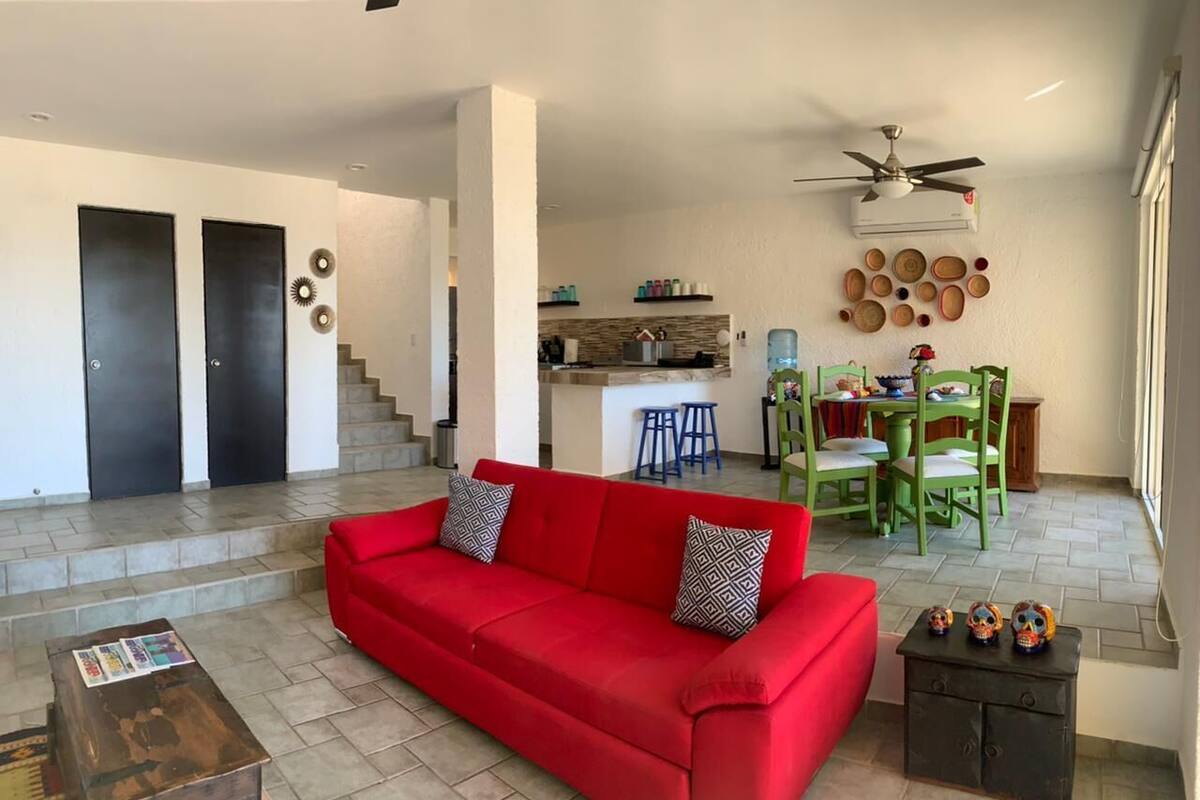 Un salón espacioso con un sofá rojo, una mesa de centro de madera y una cocina al fondo.
