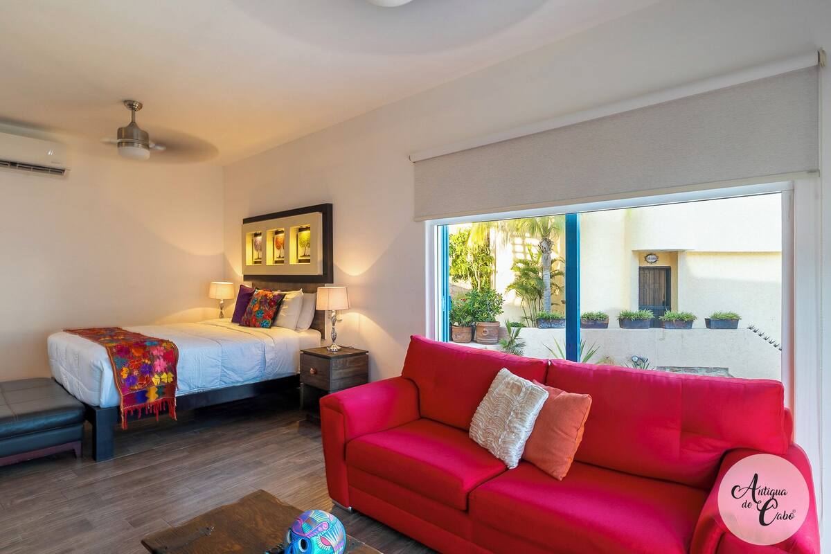 Un dormitorio con cama, mesita de noche, lámpara y un sofá rojo.