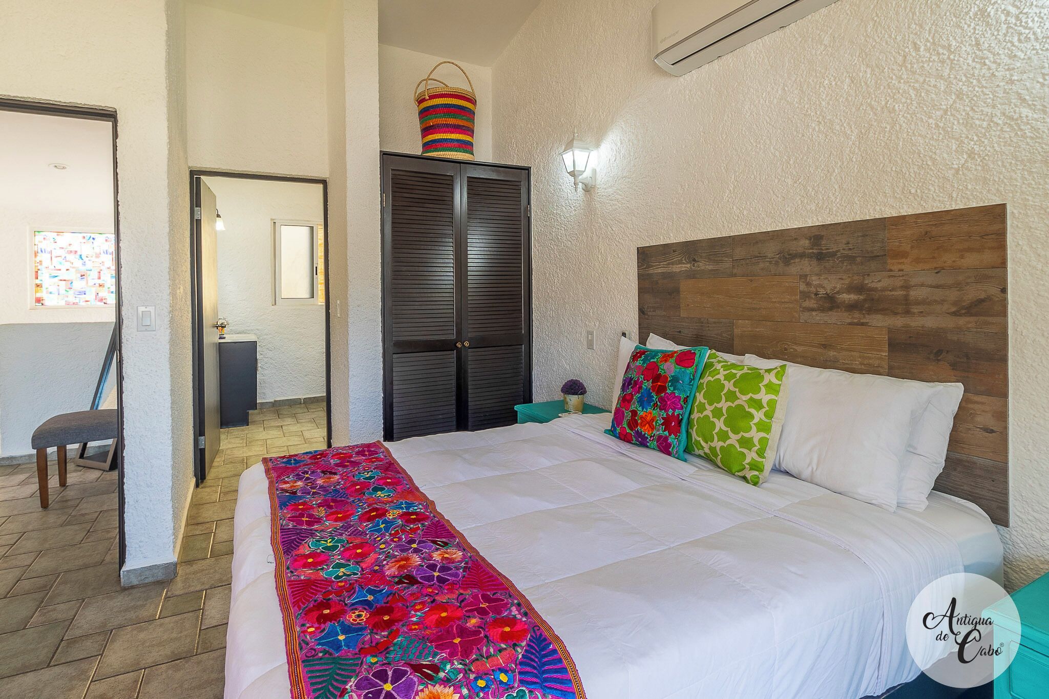 A bedroom with a bed, a wooden headboard, a colorful blanket, and a basket on the door.