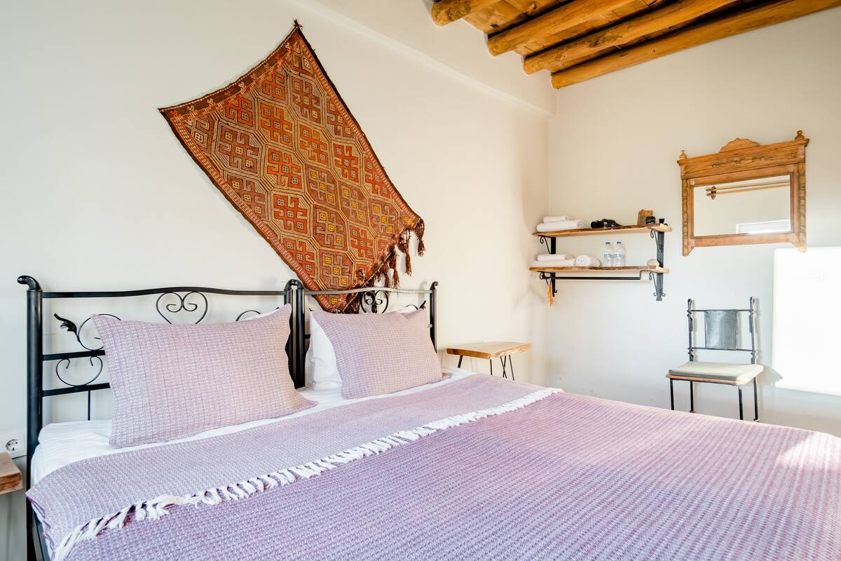 A neatly made bed with a patterned throw, a chair, and a shelf with toiletries.