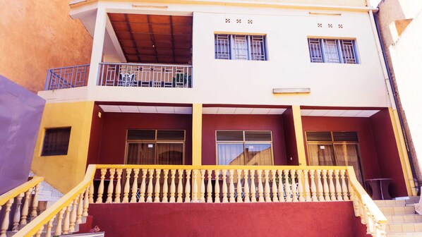 A two-story building with a balcony on the upper floor, a staircase leading to the entrance, and a red awning over the doors.