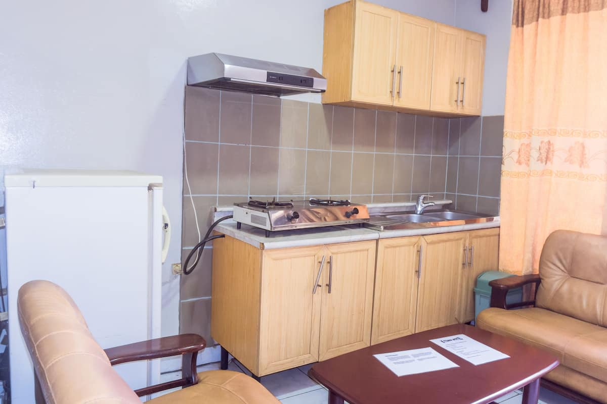 A compact kitchen with a stove, sink, and wooden cabinets. There is a small table and a chair in the living area.