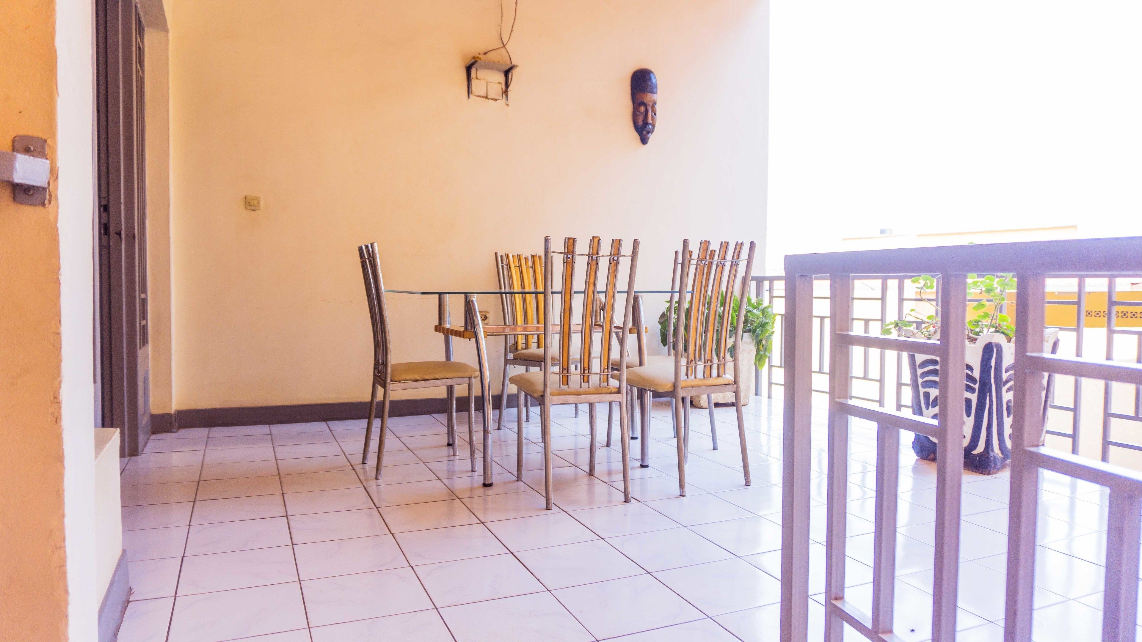 A dining area with metal chairs and a glass table, a wall-mounted light fixture, and a potted plant.