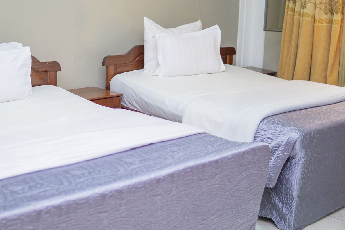 Two single beds with wooden headboards and nightstands, white bedding, and a patterned bedspread.