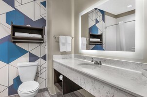 Un baño moderno con lavamanos de mármol, un espejo grande y paredes con un diseño geométrico.