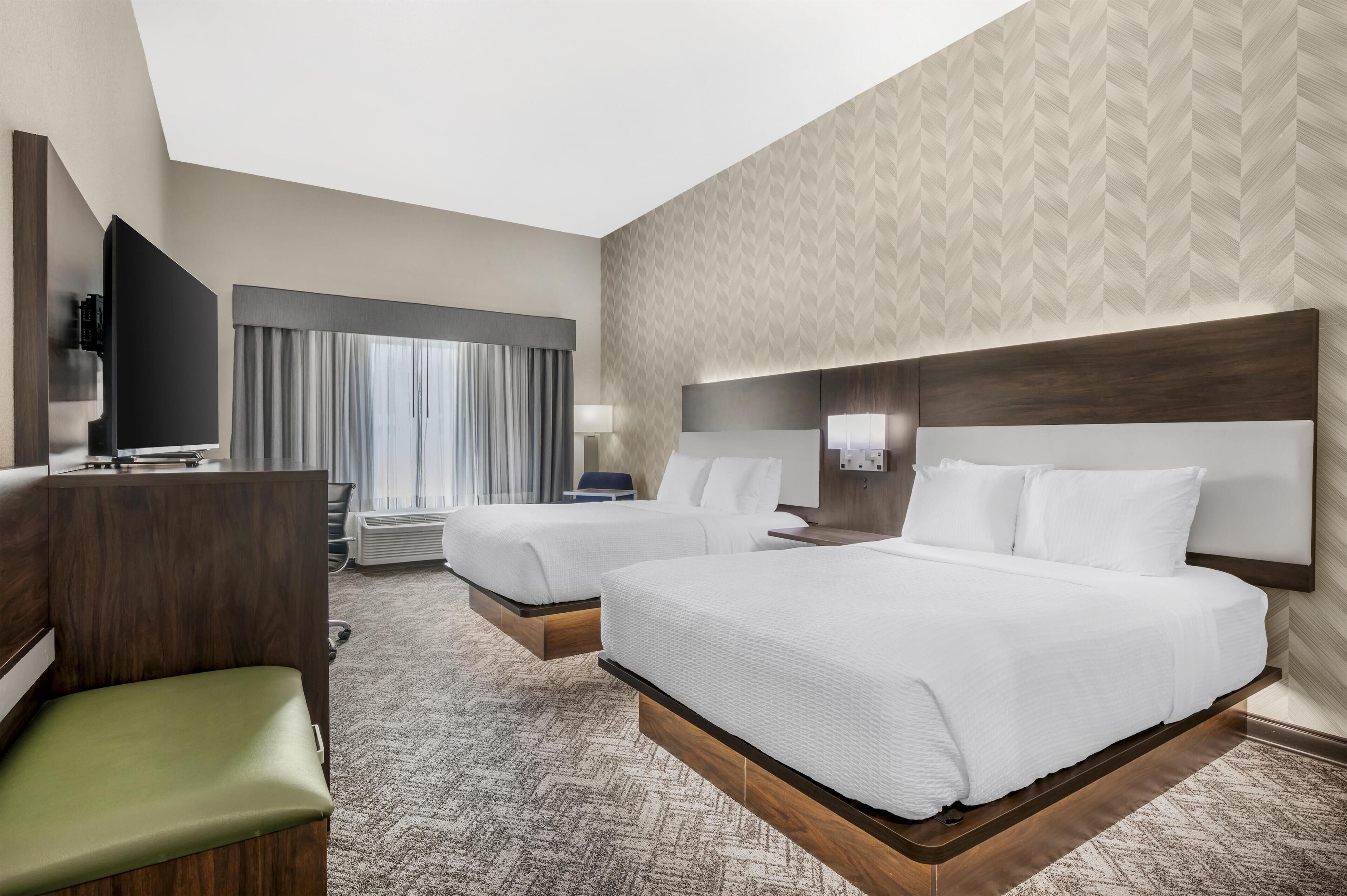A hotel room with two beds, a desk, a TV, and a seating area.