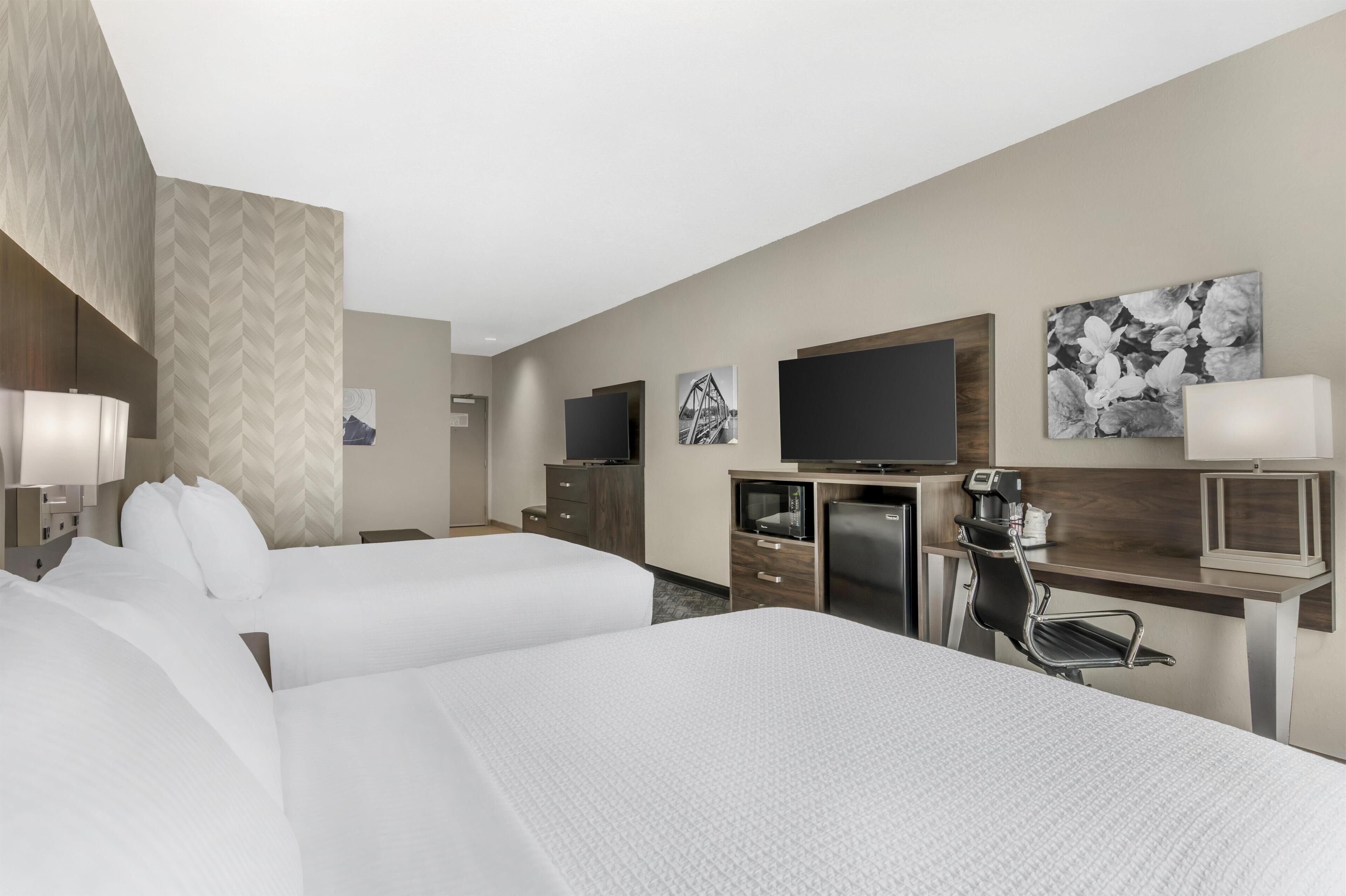 Een hotelkamer met twee bedden, een bureau met een computer, een televisie en kunst aan de muren.