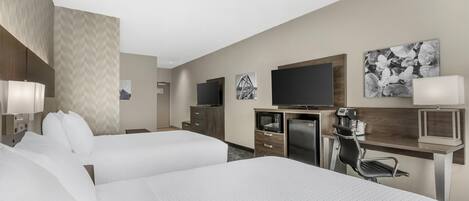 A hotel room with two beds, a desk with a computer, a TV, and artwork on the walls.