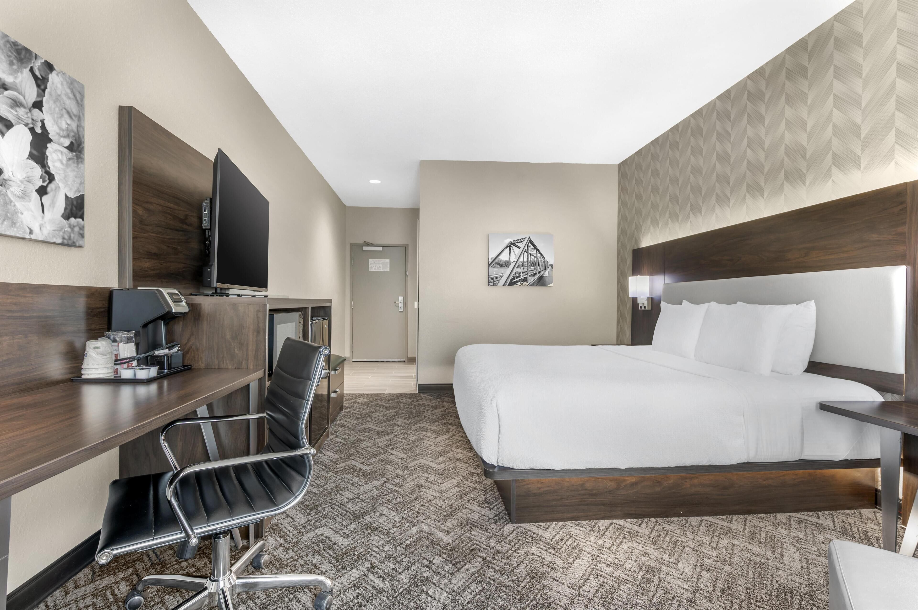 Una habitación de hotel con cama, un escritorio con silla, televisión y obras de arte en las paredes.