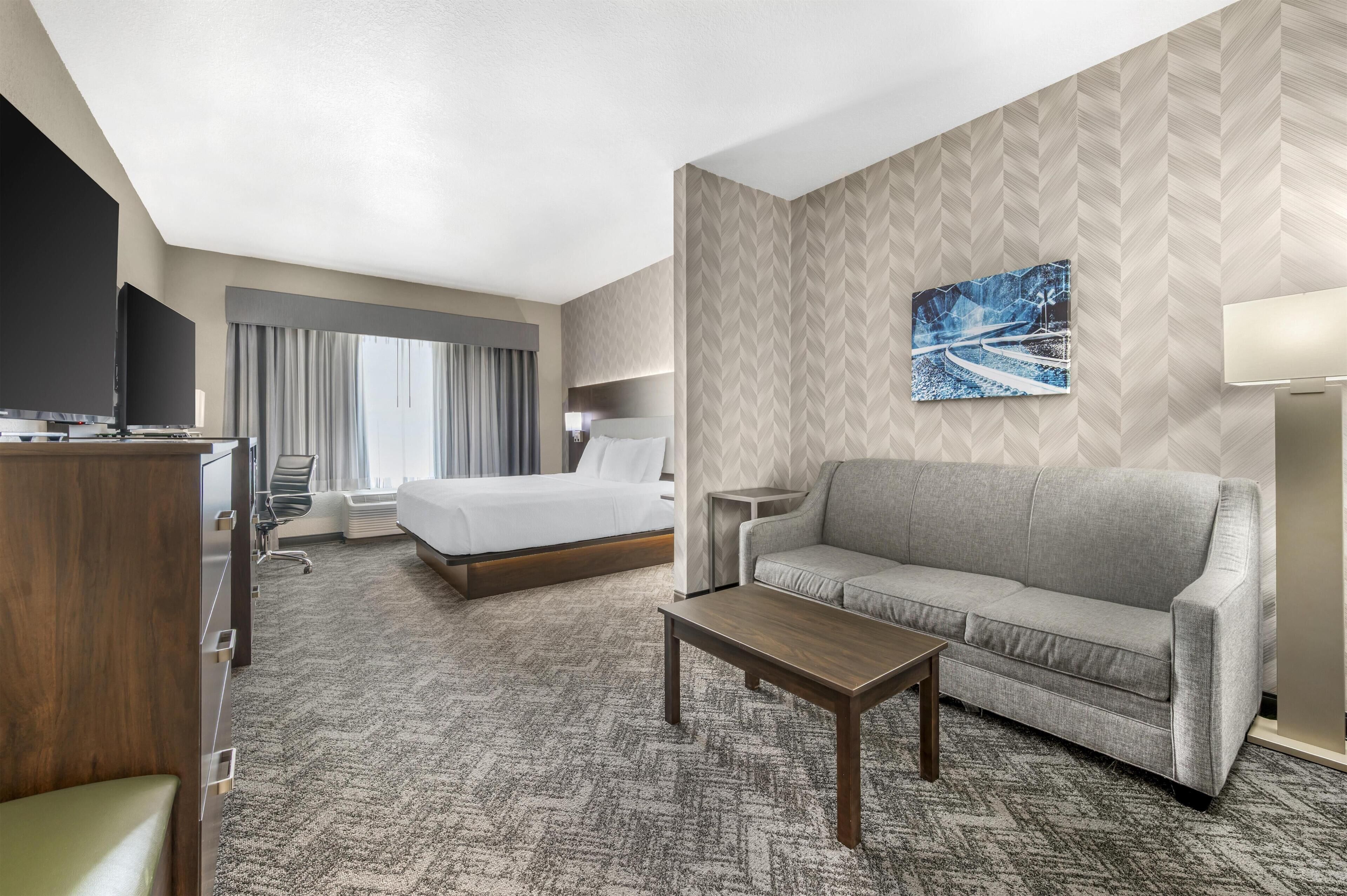 A hotel room with a bed, a sofa, a desk, and a TV.