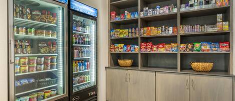 A self-service snack area with refrigerated beverage dispensers and shelves stocked with snacks and beverages.