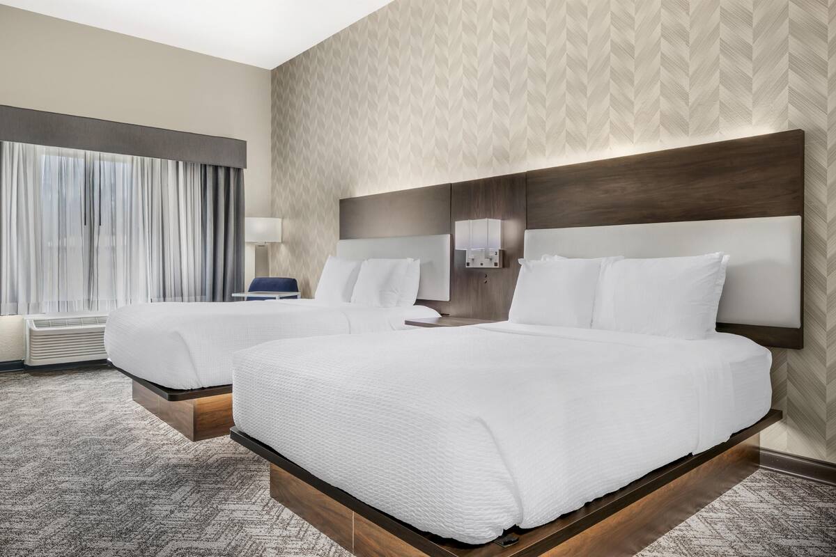 Habitació d'hotel amb dos llits, una finestra gran amb cortines, una làmpada penjada a la paret i un fons de pantalla amb disseny.