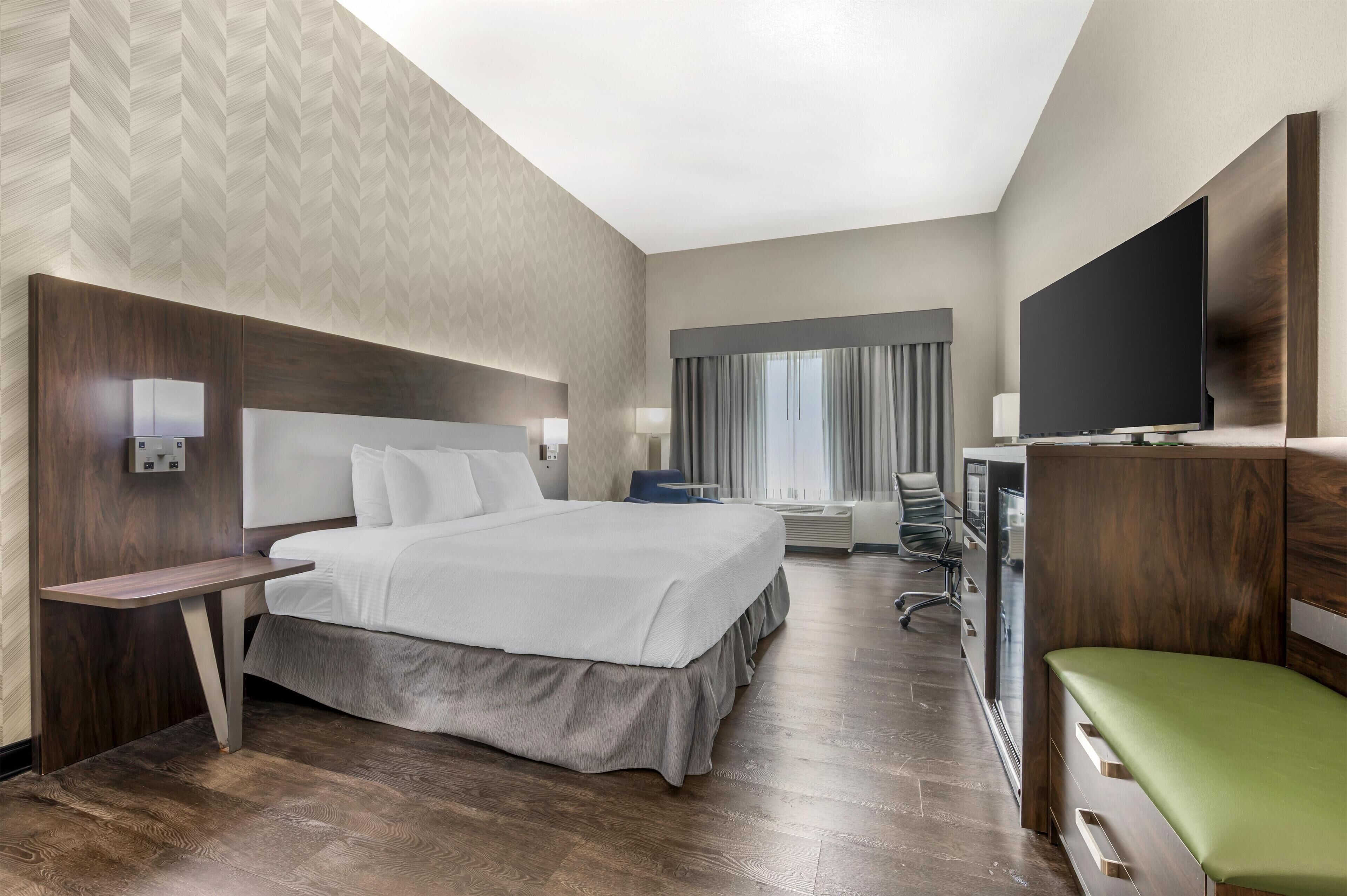Habitación de hotel moderna con una cama grande, un escritorio, un televisor y vistas al exterior.