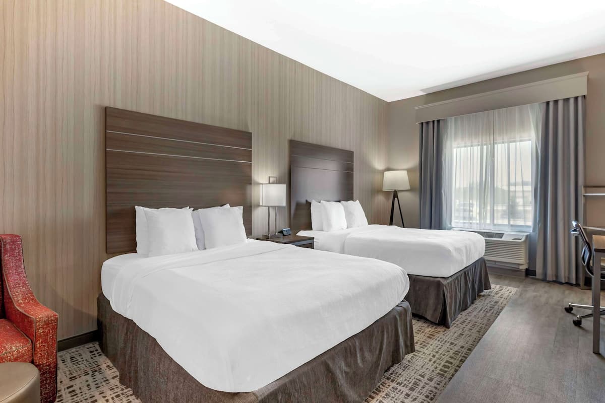 A hotel room with two beds, a desk, a chair, and a large window with curtains.