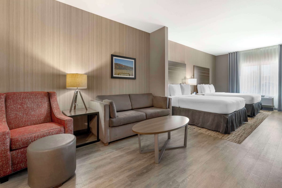 A hotel room with a sofa, a small round table, a bed with two pillows, and a framed picture on the wall.