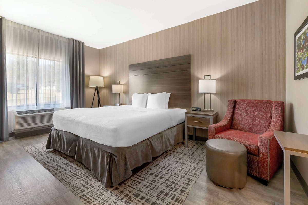 A hotel room with a large bed, a red armchair, a small table, and a bedside lamp.