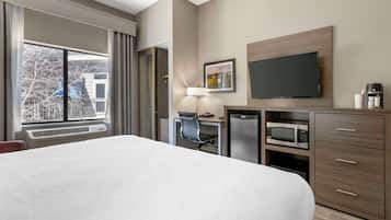 A hotel room with a large bed, a desk with a chair, a microwave, a refrigerator, a television, and a window with curtains.