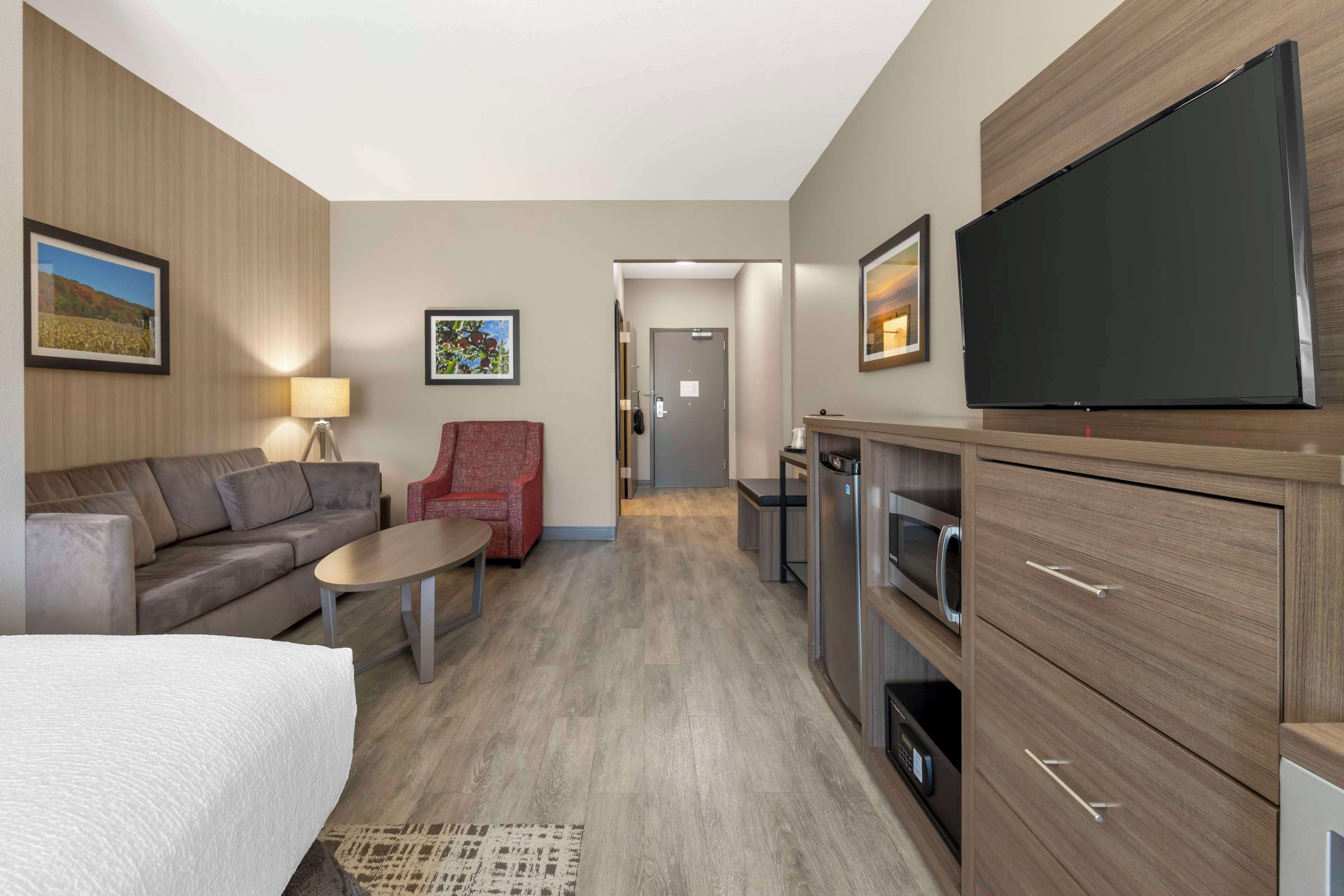 Une chambre d’hôtel comprenant un lit, un canapé, un fauteuil rouge, un téléviseur à écran plat, une table basse et un coin cuisine.