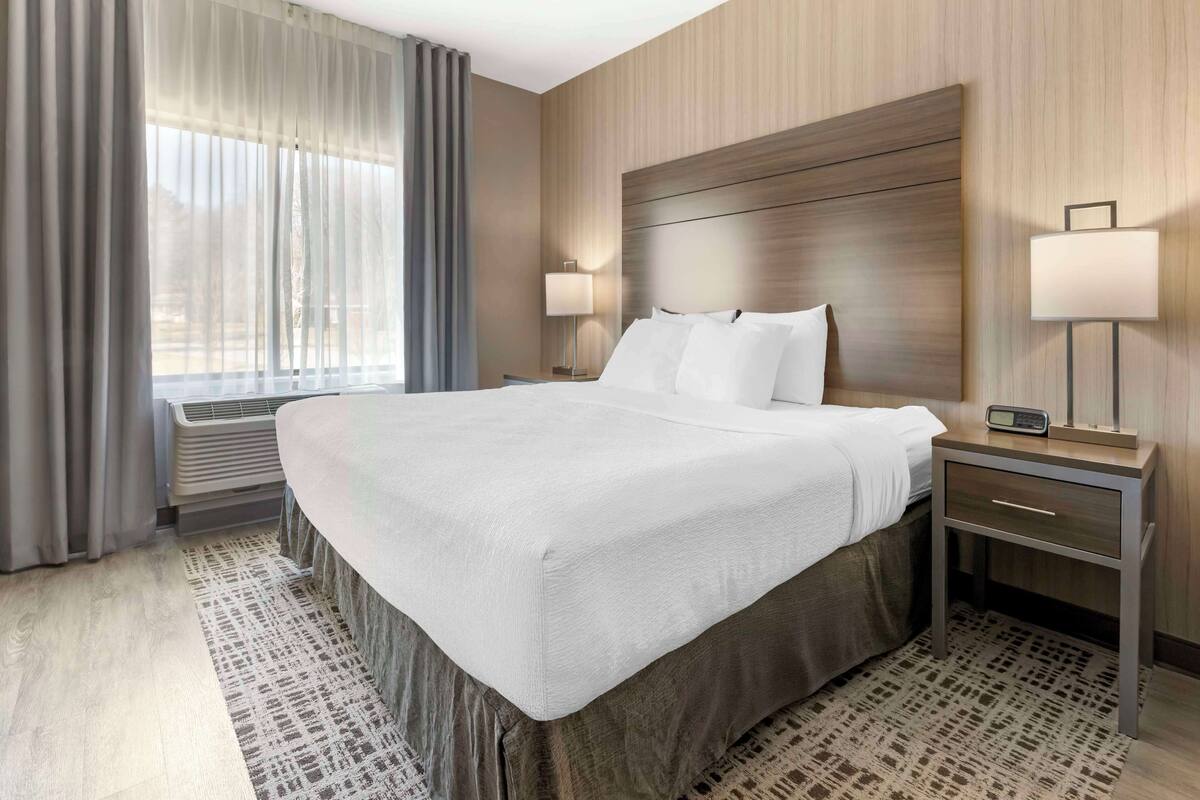 A hotel room with a large bed, two bedside tables with lamps, a window with curtains, and a patterned rug.