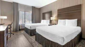 A hotel room with two beds, a desk, a chair, a lamp, and a window with curtains.
