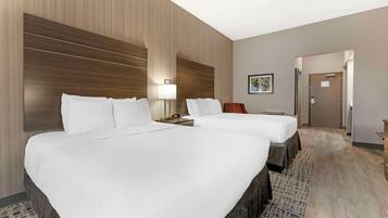 Una habitación de hotel con dos camas, una mesita de noche, una lámpara, un cuadro en la pared y una puerta que da a otra habitación.