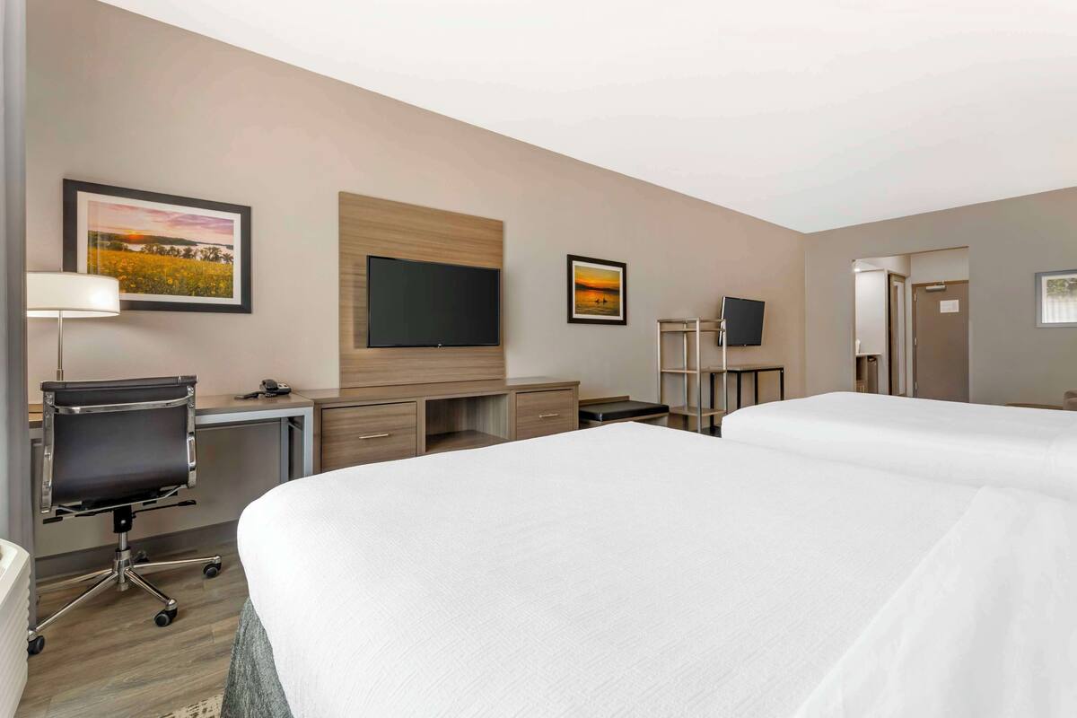 A hotel room with two beds, a desk with a chair, a flat-screen TV, and artwork on the walls.