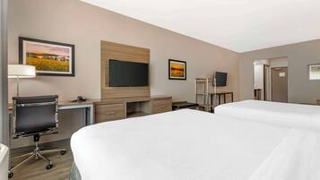 A hotel room with two beds, a desk with a chair, a flat-screen TV, and artwork on the walls.
