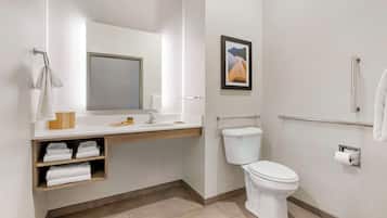 Une salle de bain moderne avec des toilettes, un lavabo et un miroir. On y trouve des étagères avec des serviettes et un tableau encadré accroché au mur.
