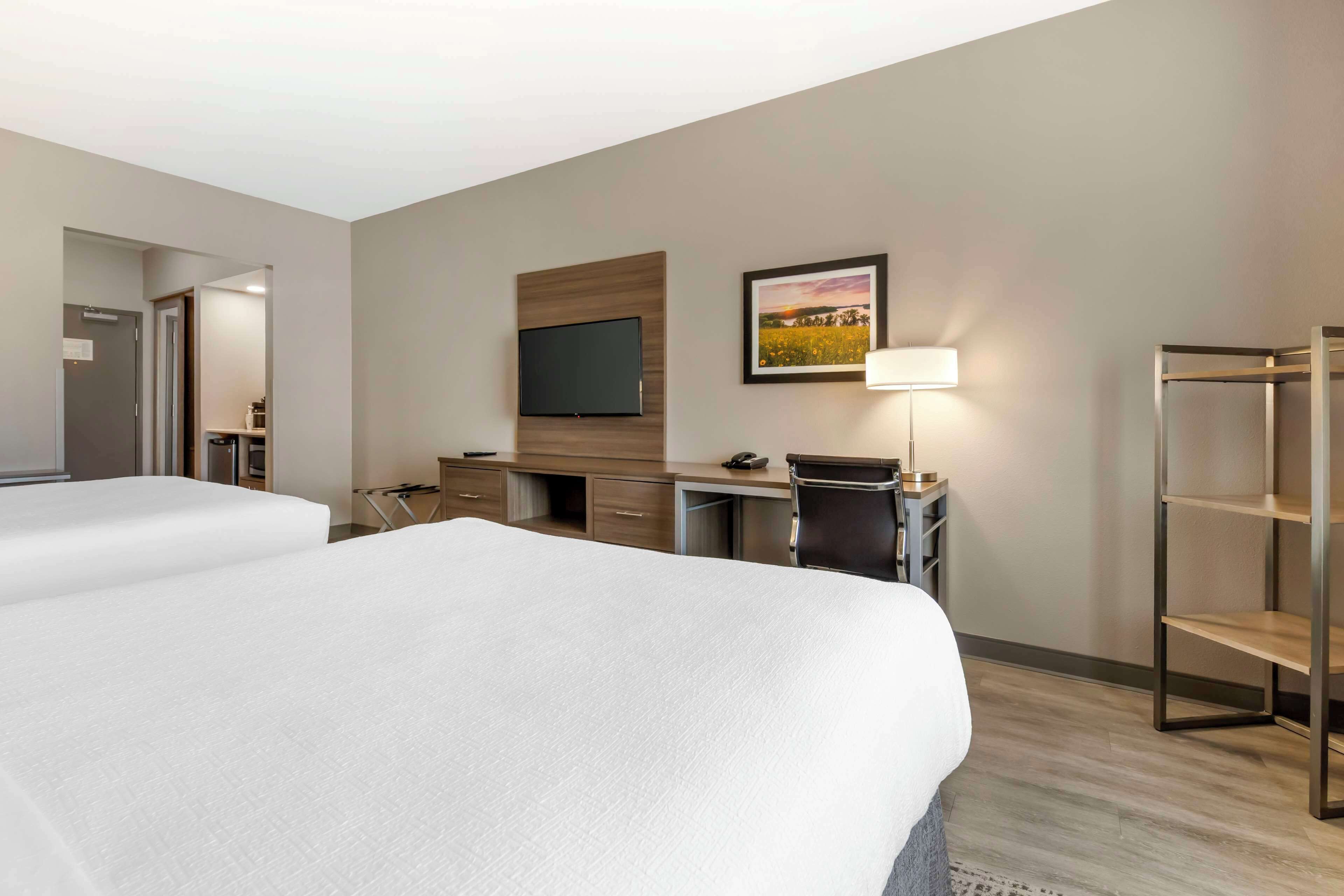 A hotel room with two beds, a desk, a TV, a lamp, and a bookshelf.