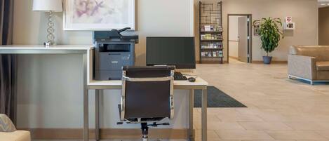 A modern hotel lobby with a reception desk, a computer, a printer, a desk chair, a sofa, a potted plant, and a bookshelf.