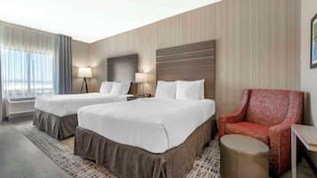 A hotel room with two beds, a red armchair, a small table, and a patterned rug.