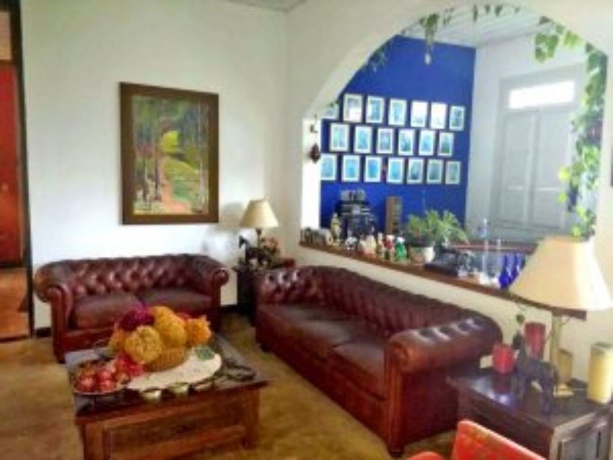 A living room with a brown leather sofa, a coffee table with fruits, and a wall decorated with framed pictures.