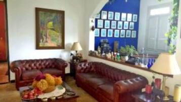 A living room with a brown leather sofa, a coffee table with fruits, and a wall decorated with framed pictures.