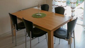 Un coin repas avec une table en bois, des chaises noires, un luminaire suspendu et une fenêtre ornée de rideaux à rayures.