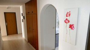 Un couloir avec des armoires en bois, une porte blanche et une œuvre d’art florale encadrée accrochée au mur.