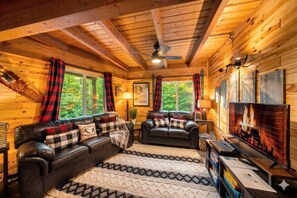 Ein gemütliches Cabin-Interieur mit Kamin, Ledersofas und einem großen Fenster mit Blick auf Grünflächen.