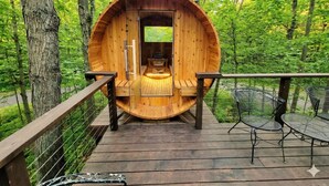 A wooden cabin with a circular design, a wooden deck, and metal chairs. - Chalet in the Trees - Sauna|Game Room|Pool Access (Bellaire)