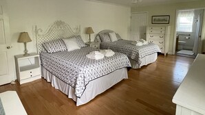 Ein Schlafzimmer mit zwei Betten, einem Deckenventilator, einem Nachttisch mit Lampe, einer Kommode und einer Badezimmertür.