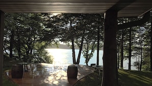 An outdoor seating area with tables and chairs, overlooking a body of water and surrounded by trees. - Lakefront Hideaway (Litchfield)