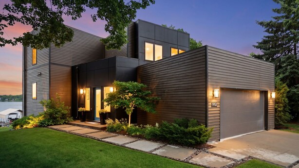 A modern two-story house with a garage, a well-maintained lawn, and a driveway leading to the entrance. - Lakefront Luxury (Mound)
