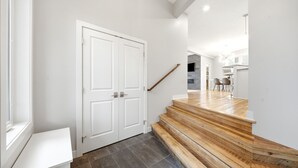 Una escalera de madera lleva a un rellano en el segundo piso, con una puerta blanca y un banco.