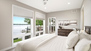 A bedroom with a bed, a dresser, a ceiling fan, and large windows with a view of a dock and water. - Lakefront Luxury (Mound)
